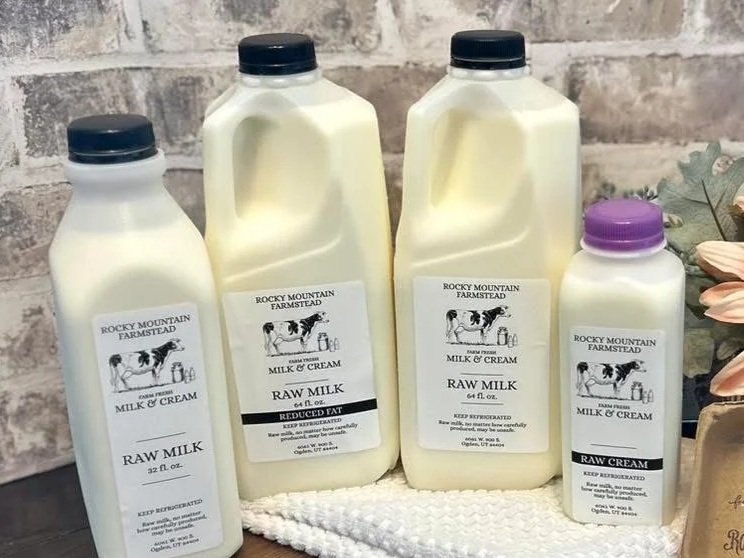 Bottles of raw milk and cream from Rocky Mountain Farmstead displayed against a rustic backdrop, showcasing various sizes including reduced fat options. The labels emphasize freshness and the need for refrigeration, appealing to health-conscious consumers.