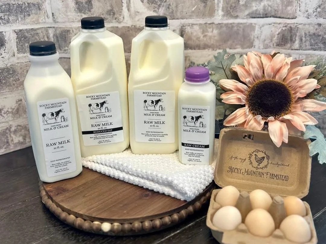 Bottles of raw milk and cream from Rocky Mountain Farmstead displayed on a wooden platter, accompanied by a carton of farm-fresh eggs and a decorative sunflower, highlighting natural dairy products and farm goods.